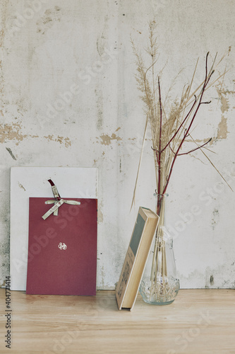 still life in the form of a glass transparent vase with dried grass and books on the background of a vintage wall (ID: 404771414)