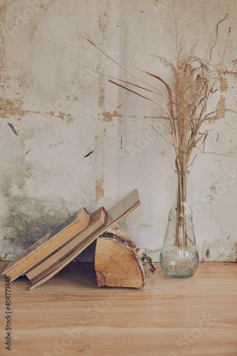still life in the form of a glass transparent vase with dried grass and books on the background of a vintage wall