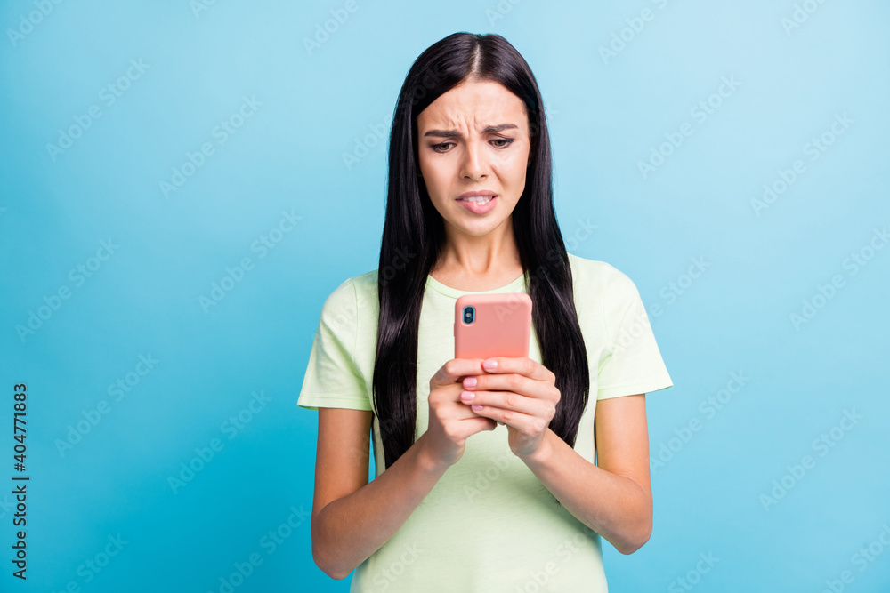 Photo portrait of unhappy woman biting lower lip holding phone in two hands isolated on pastel blue colored background Photo portrait of unhappy woman biting lower lip holding phone in two hands isolated on pastel blue colored background