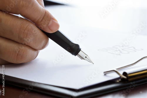 Hand of businessman with pen writing business plans 2021 on white paper.