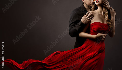 Romantic Lovers Couple Dancing. Man hugging and kissing beautiful Woman in Silk Red flying Dress. Fashion Portrait. Studio Black Background