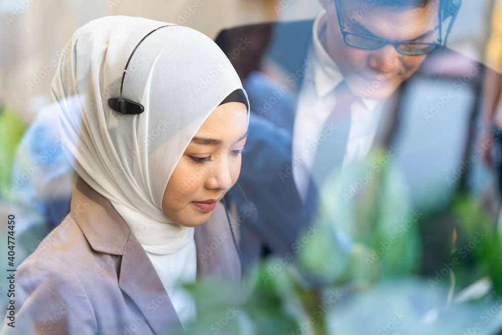 Naklejka premium Muslim call center staff. The customer service manager is assisting the call center clerk to provide customer support services. The young call center is working to answer customer questions. Trainee