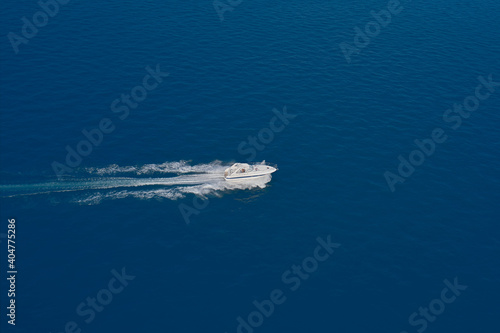 Aerial view of a boat in motion on blue water. Top view of a white boat sailing in the blue sea. Drone view of a boat sailing at high speed. luxury motor boat. © Berg