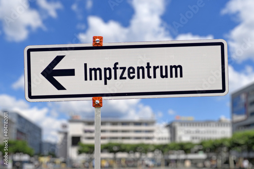German street sign pointing towards vaccination center called 'Impfzentrum' set up to vaccine people against Corona virus in fornt of blurry city background