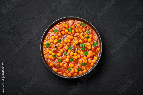 Chana Masala or Chole in black bowl on dark slate table top. Indian cuisine veg chickpeas curry dish. Asian spicy vegetarian food and meal. Top view
