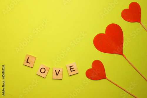 Three red hearts on a yellow background. The word love. View from above. Hearts are on the right. The concept of Love. Valentine is Day. Romance. Background. Texture. Copy space. Flatlay.
