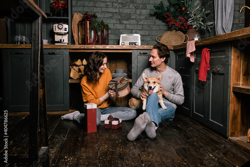 Happy caucasian couple on the kitchen floor with their corgi dog. Young family, woman and man giving each other gifts. Valentines day