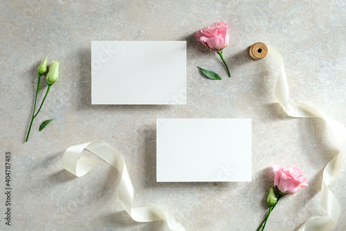 Blank paper cards, flowers, ribbon on stone table. Wedding invitation cards templates. Flat lay. Top view.