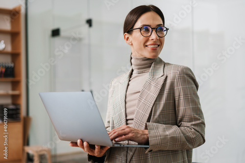 фотографія Smiling charming woman in eyeglasses working with laptop at office