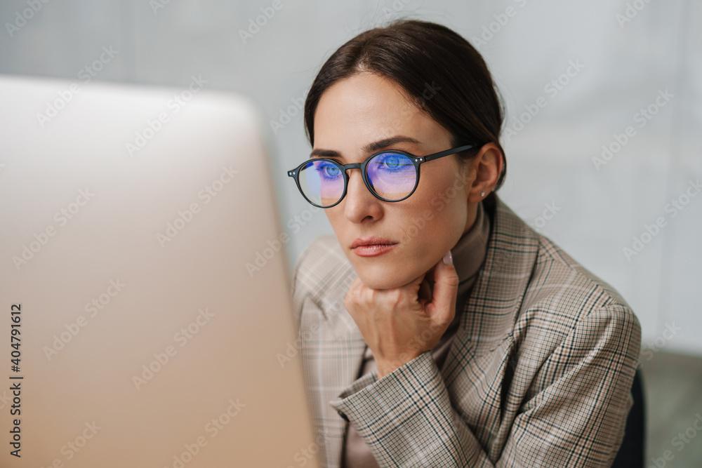 Focused charming woman in eyeglasses working with computer in office Focused charming woman in eyeglasses working with computer in office