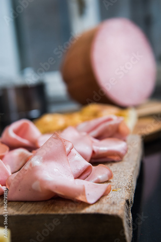 Mortadella Bologna is a large Italian sausage made with cooked pork, mixed with cubes of cylindrical or oval-shaped pork fat. Slices of mortadella on a wooden cutting board