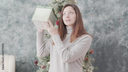 A beautiful woman holds a box with a gift at the Christmas tree at home. photo