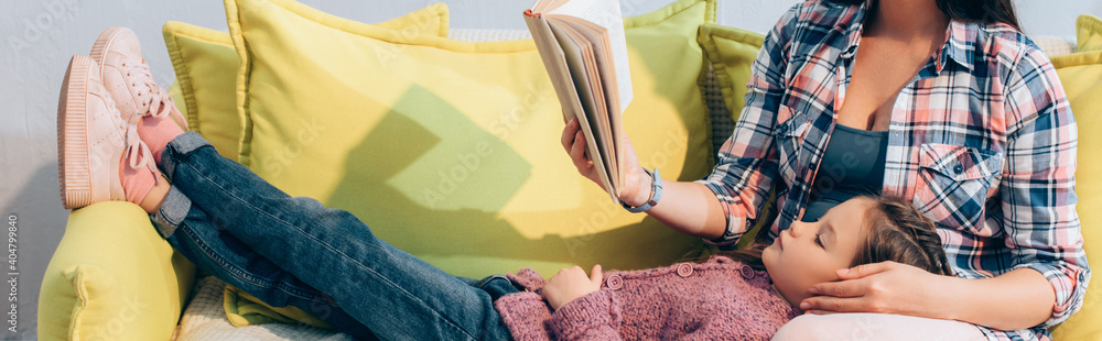 Εκτύπωση καμβά Daughter with crossed legs lying near mother with book on couch, banner