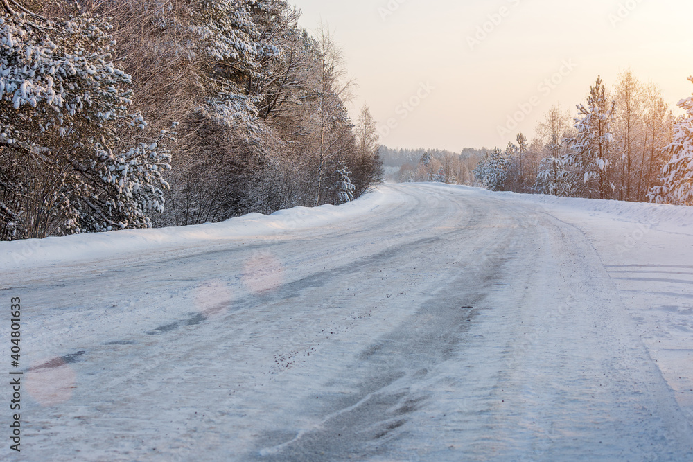 Fototapeta premium winter, icy road in the snow. Turning the road. Trees in snow and sunshine. Horizontal photo. Winter travel.