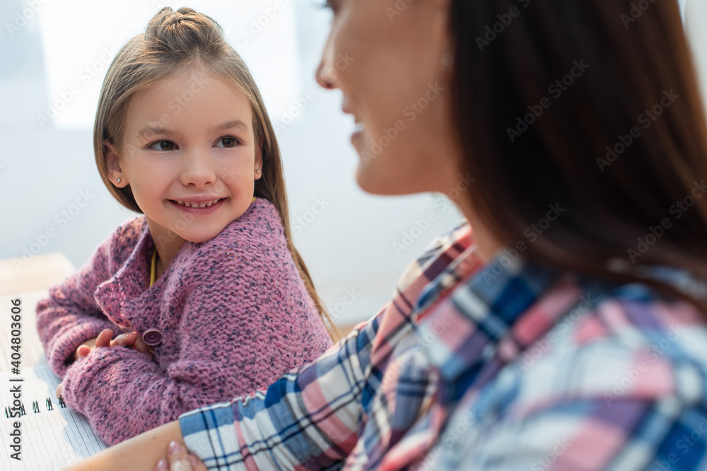 Smiling daughter looking at blurred mother on foreground Smiling daughter looking at blurred mother on foreground