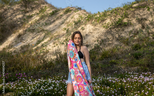 Balneário Gaivota, Santa Catarina, Brazil, November 2020. Model looking to the left side holding a beach sarong printed next to her face with flowers and dunes in the background. photo