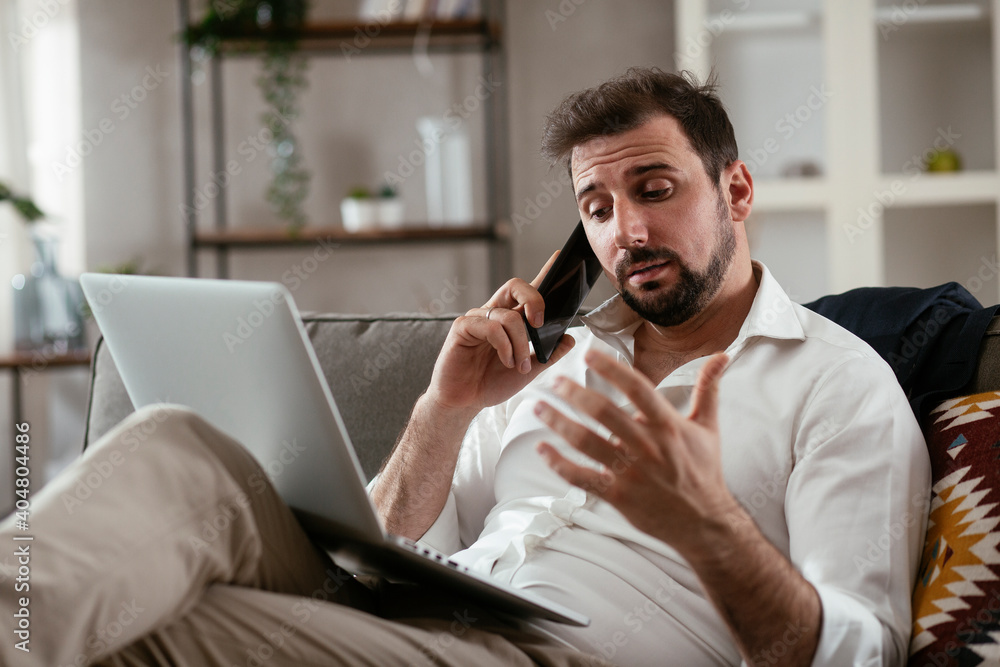 Young man working from home. Businessman at home on sofa with laptop and phone... Young man working from home. Businessman at home on sofa with laptop and phone...