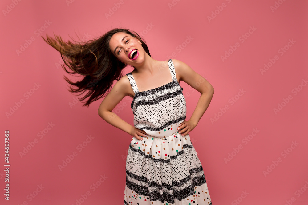 Studio shot of happy dancing lady in summer dress with flying hair over pink background Studio shot of happy dancing lady in summer dress with flying hair over pink background