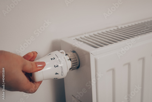 A woman's hand turns the battery heating knob. Heating in an apartment, at home. Heating prices.