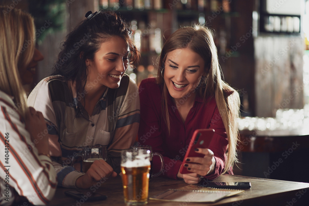Three happy girlfriends are having fun time in pub. They are talking and drinking beer. Friendship concept. Three happy girlfriends are having fun time in pub. They are talking and drinking beer. Friendship concept.