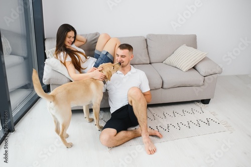Happy Loving Family Concept. Portrait of beautiful couple with dog sitting on the floor in modern apartment