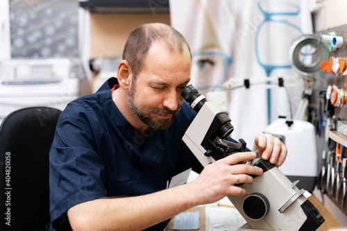 Ophthalmologist produces customed lenses for glasses. Man works with microscope.