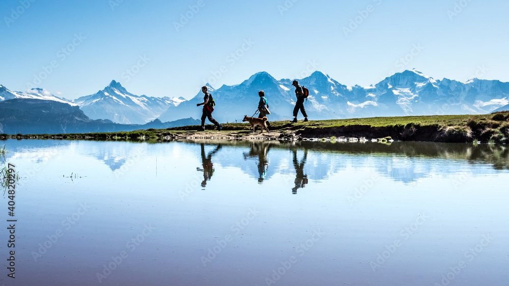 Wandergruppe mit Hund gespiegelt in einem kleinen Bergsee vor der Kulisse vom berner Oberland, Alpen, Schweiz