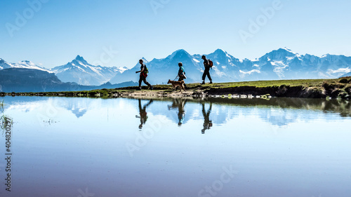 Wandergruppe mit Hund gespiegelt in einem kleinen Bergsee vor der Kulisse vom berner Oberland, Alpen, Schweiz
