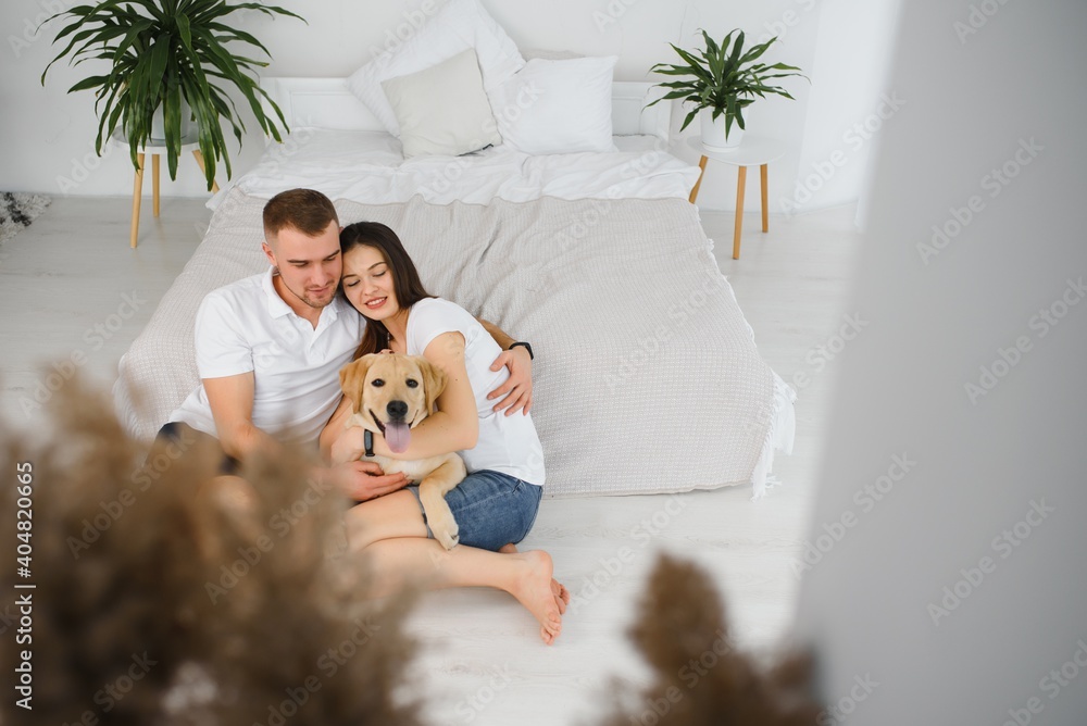 Young couple with a dog at home. Young man and a woman playing at home with dog. Young couple with a dog at home. Young man and a woman playing at home with dog.