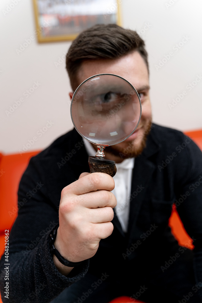 Funny man looks through magnifying glass in clinic. Funny patient in hospital. Funny man looks through magnifying glass in clinic. Funny patient in hospital.