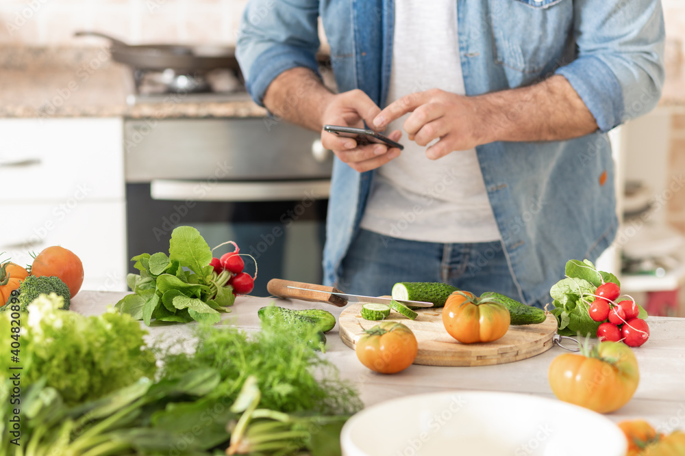 Man with phone in his hands, looks at recipe and prepares healthy lunch or dinner