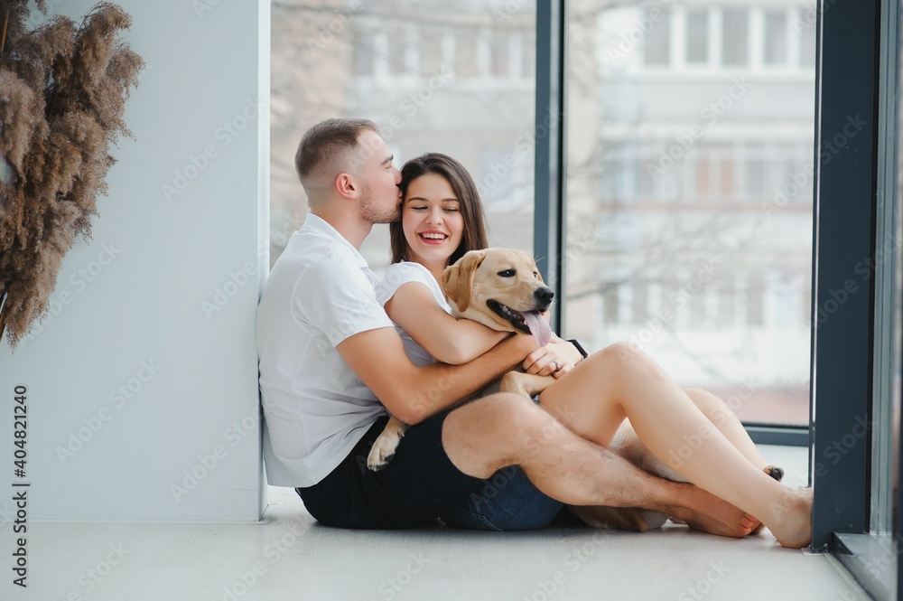 Young couple with a dog at home. Young man and a woman playing at home with dog.