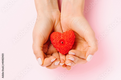 Female hands with gentle manicure hold a heart-shaped candle. Pink background and St.Valentine's day concept.