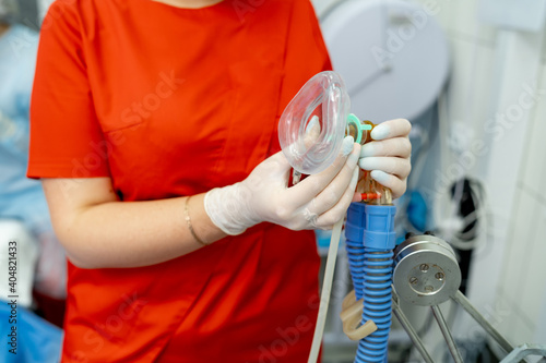 Breathing anaesthesiology face mask held in hands in latex transparent gloves. Attach filter visible. Clinic background.