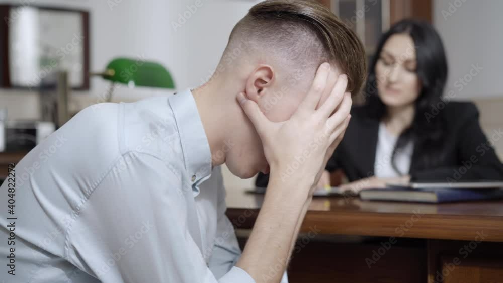 Side view of frustrated desperate young man holding head in hands rocking on chair in psychologist office. Depressed Caucasian patient with nervous breakdown on psychological consultation. Side view of frustrated desperate young man holding head in hands rocking on chair in psychologist office. Depressed Caucasian patient with nervous breakdown on psychological consultation.