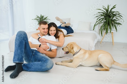Smiling man and woman sitting on floor at home with their pet dog. Portrait of happy dog loving family with their pet dog. © Serhii