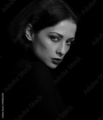 Sexy vamp woman with bright evening makeup, red lipstick brown brow posing isolated on dark black background. Closeup portrait in deep low key light shadows.