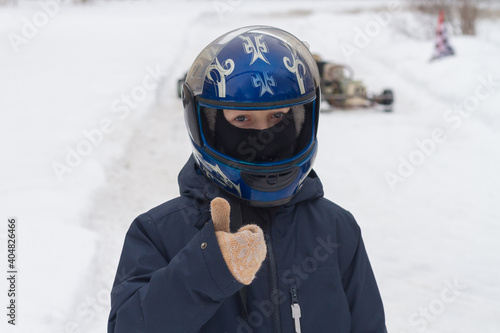 A boy in winter on the track in a helmet is waiting for karting competitions.