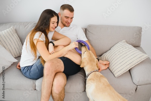 Guy and his girlfriend are resting in bedroom. Happy couple lovingly looking at their pet who wants to play