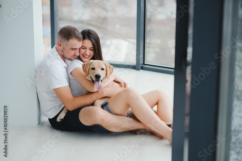 Young beautiful couple with dog sitting on the floor at new home. © Serhii
