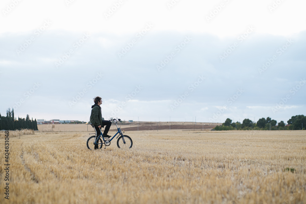 Young man with vintage bicycle observing a dry field in the countryside