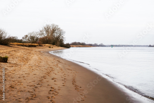 the river in the winter, sand beach on a cloudy day, calm water