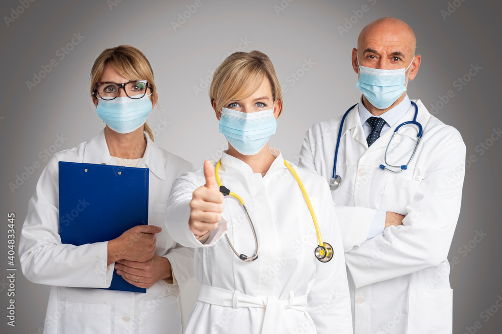 Studio shot of medical team wearing face masks and female doctor giving thumbs up Studio shot of medical team wearing face masks and female doctor giving thumbs up