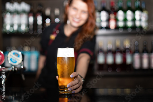 Portrait of attractive female bartender tapping beer in pub, focus on hands holding beer