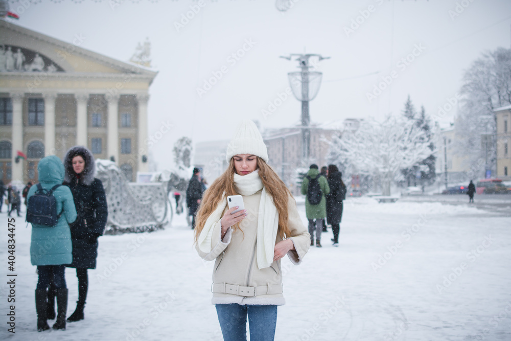 Stylish beautiful girl in warm clothes with coffee and a phone in her hands posing for a photographer on a city street