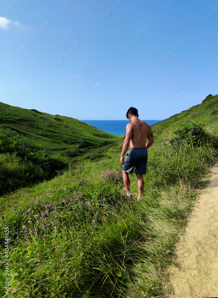 Hombre sin camiseta en pradera frente al mar