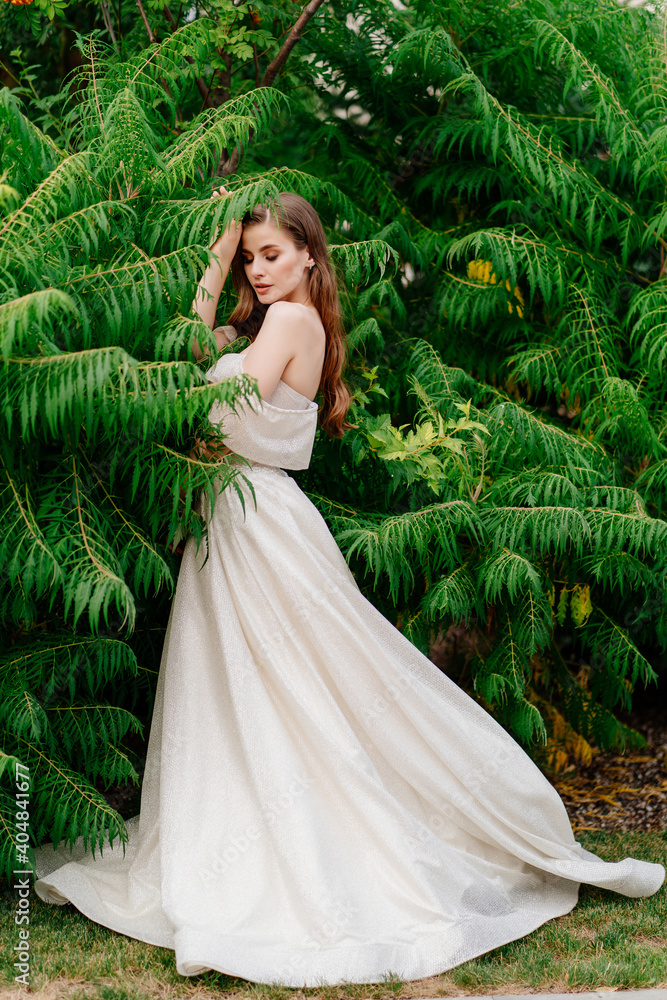 beautiful woman in a white dress posing in against of green leaves.