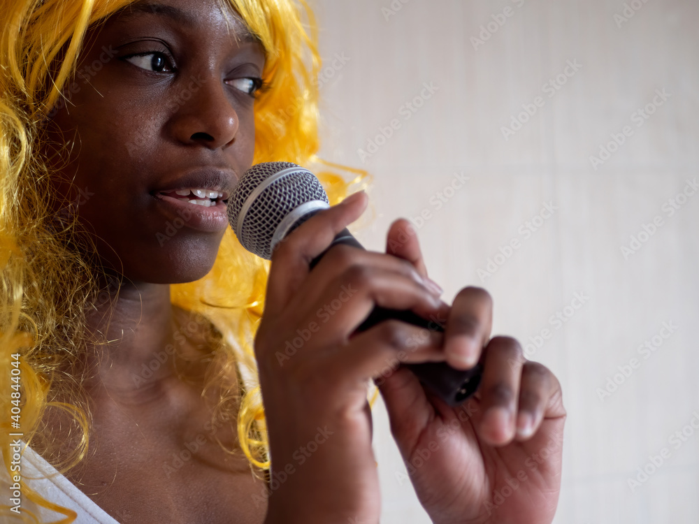 Φωτογραφία African american woman in white t-shirt in bright yellow wig sings karaoke with