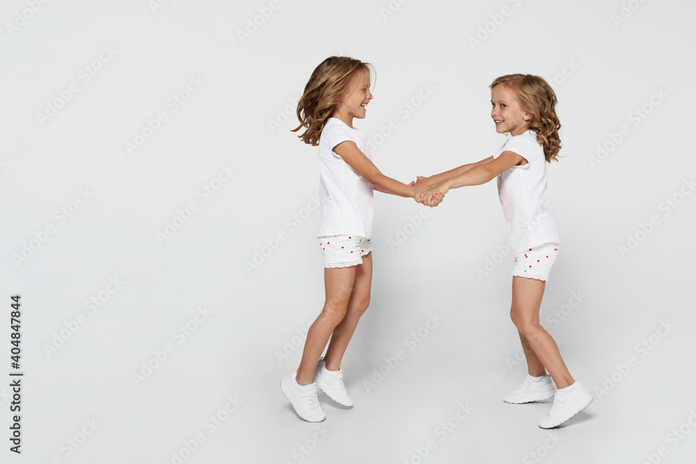 Happy funny little twin sisters in white clothes dancing isolated on white background. Happy funny little twin sisters in white clothes dancing isolated on white background.