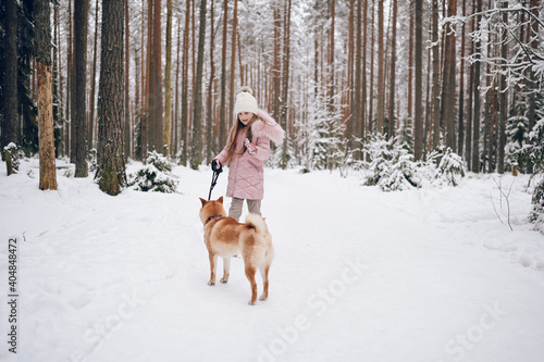 Fototapeta Naklejka Na Ścianę i Meble -  Happy family weekend - little cute girl in pink warm outwear walking having fun with red shiba inu dog in snowy white cold winter forest outdoors. Kids sport vacation activities concept.